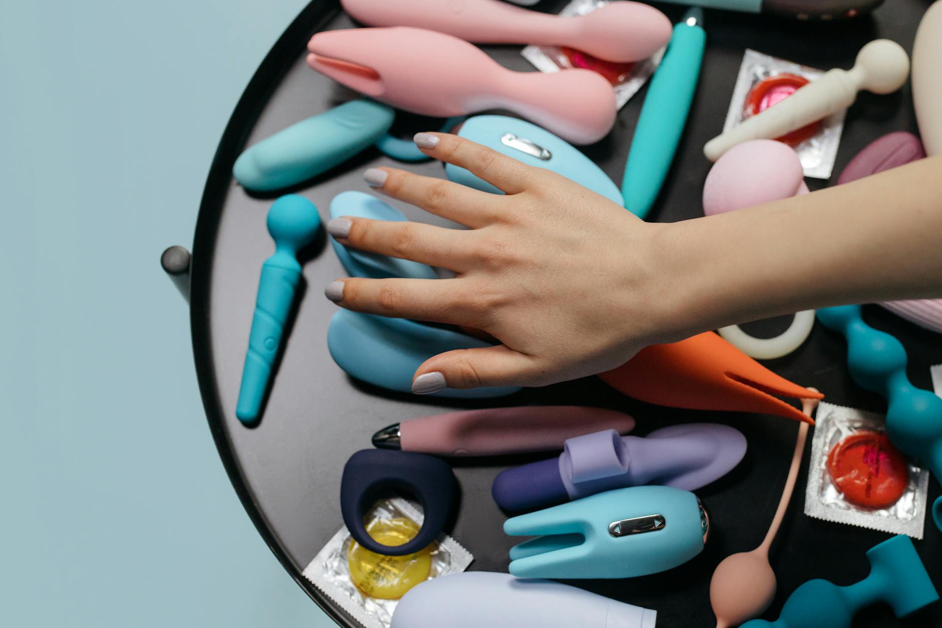 A hand reaching over a variety of colorful adult toys arranged on a table