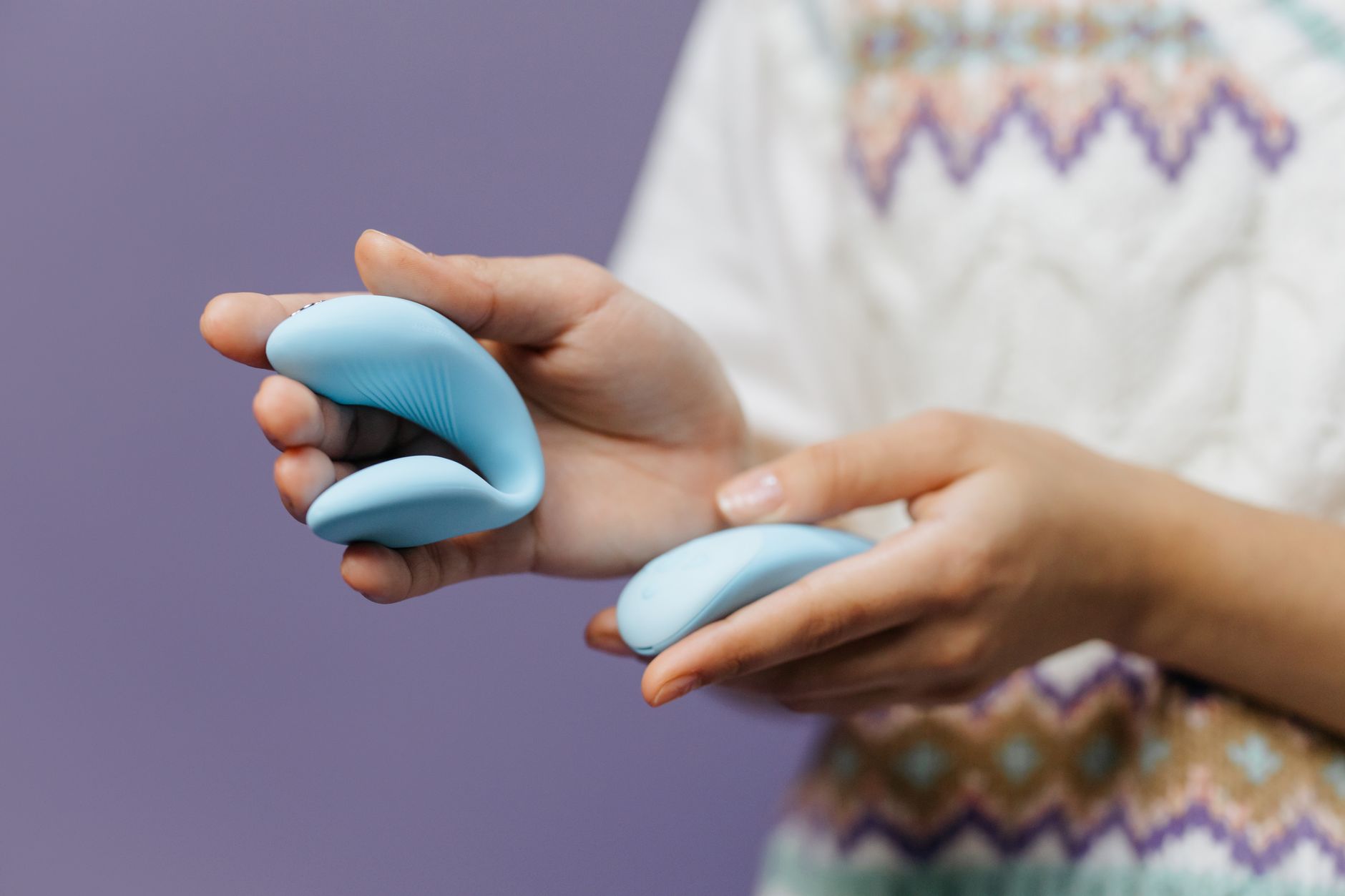 Hands holding a sleek blue vibrator against a purple background, symbolizing solo pleasure and self-reconnection after conflict.