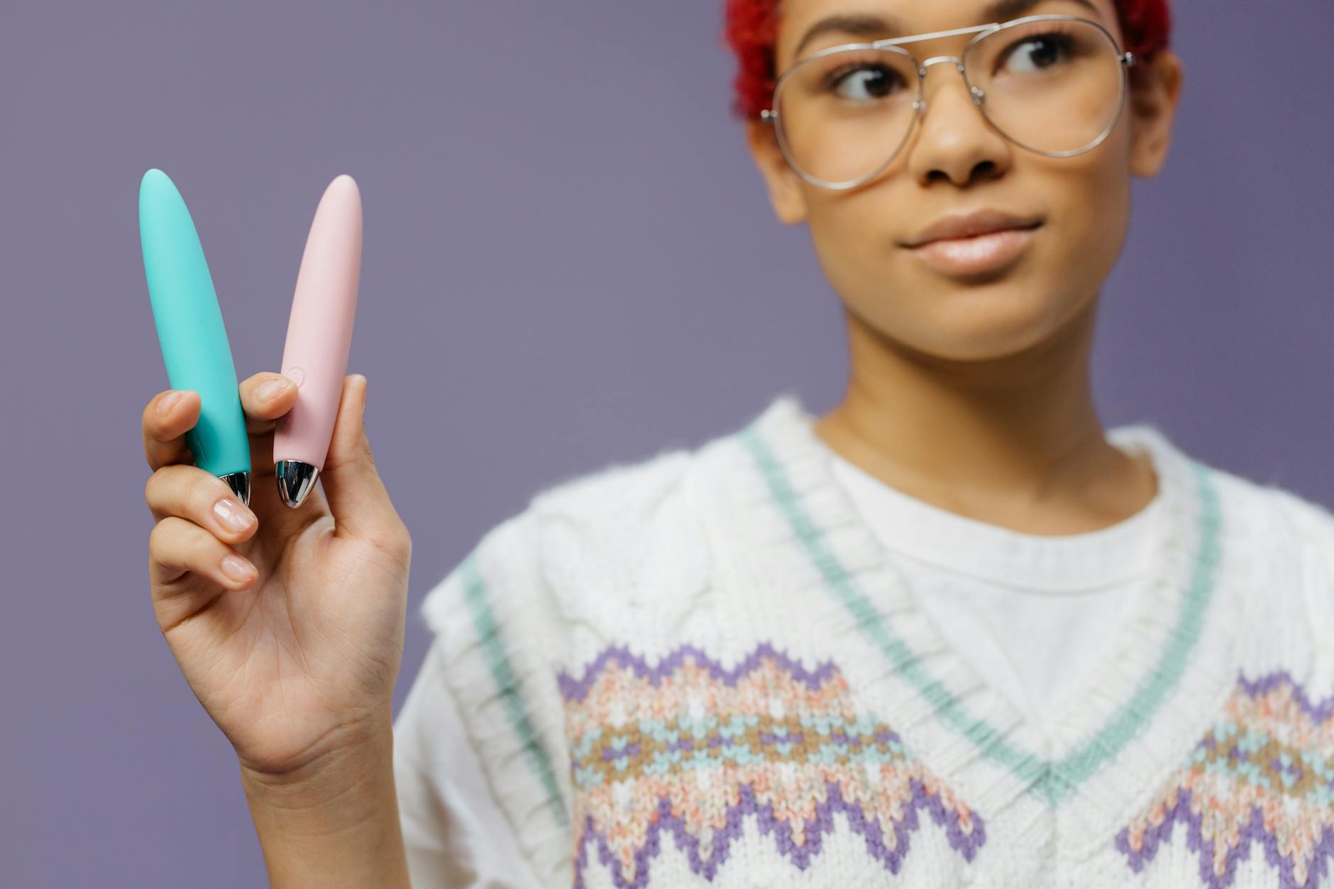 Colorful clitoral vibrators held against a purple background, symbolizing pleasure and self-care