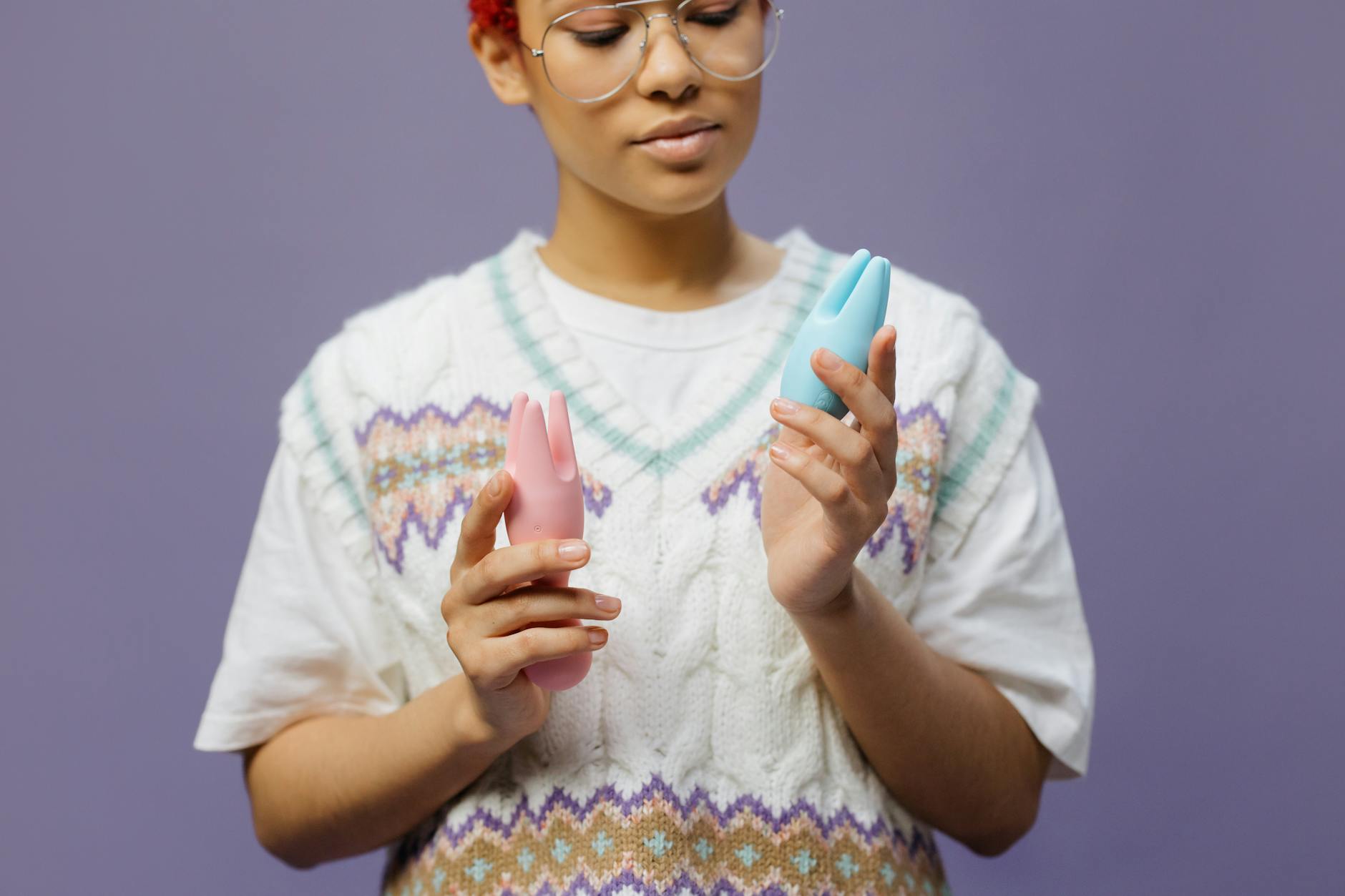 Woman holding a pink and blue clitoral vibrator in a thoughtful moment of personal exploration