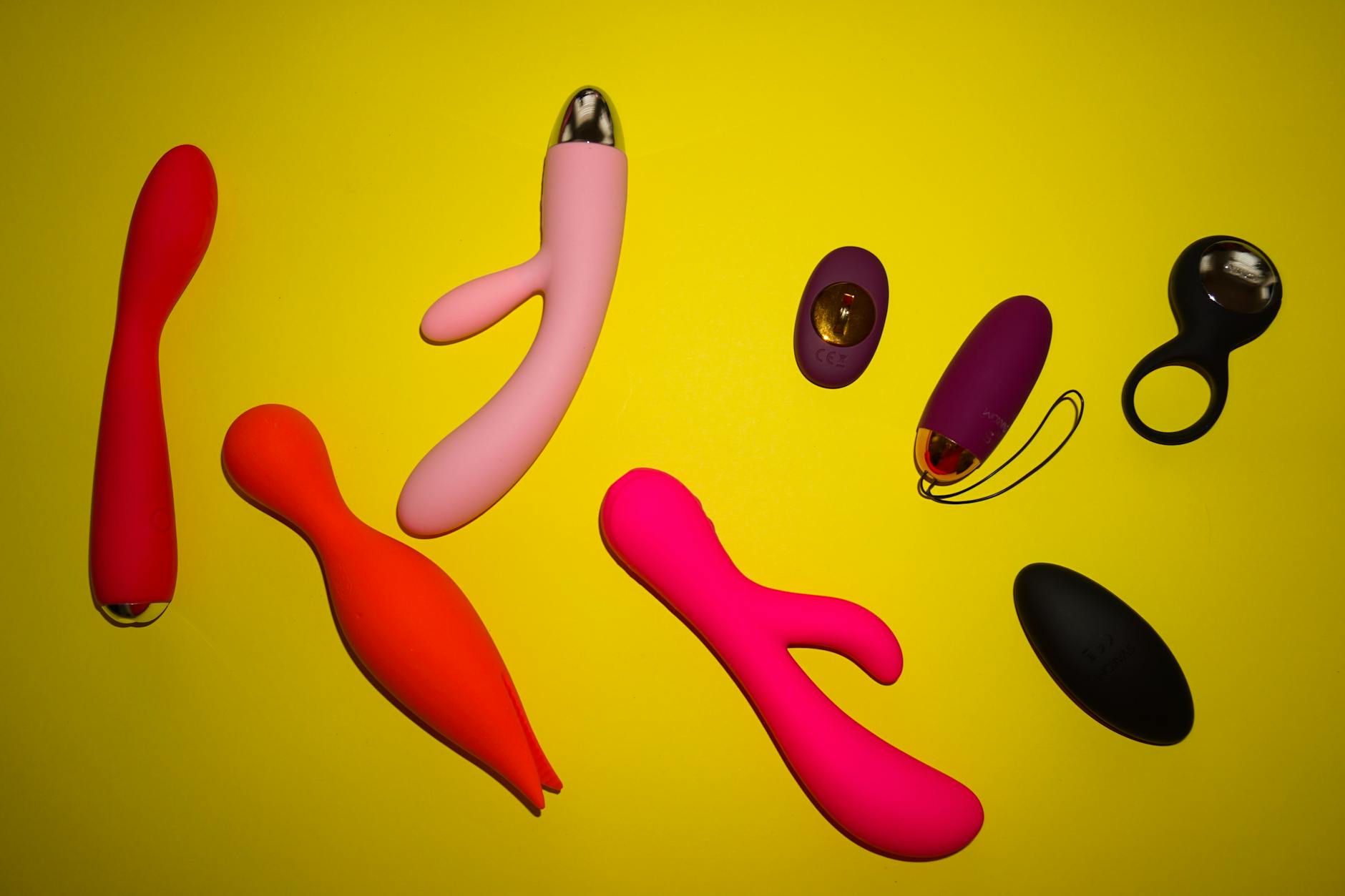 A hand holding a basket with colorful vibrators and a pink flower against a soft background