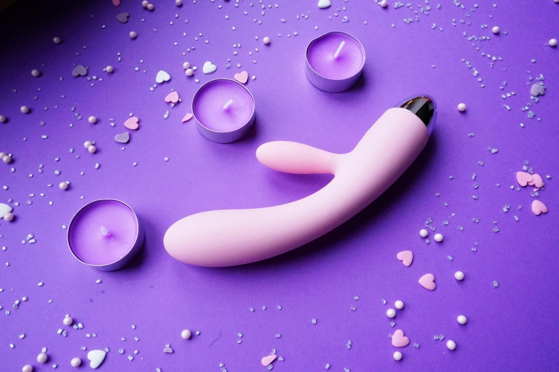 Vibrator surrounded by candles and rose petals on purple surface, symbolizing sensitive pleasure